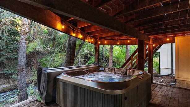 Un bain à remous situé dans un espace extérieur abrité, doté d’une structure en bois, et entouré d’arbres et d’un chemin en briques.