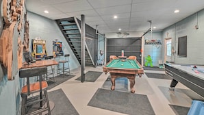A pool table, chairs, a staircase, and arcade games in a room with a modern design. - Lake Luzerne Home w/ Fire Pit on Hudson River (Lake Luzerne)