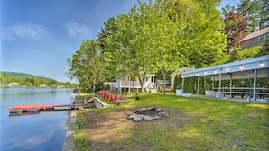 A lakeside property with a covered patio, a fire pit, and a dock with boats. - Lake Luzerne Home w/ Fire Pit on Hudson River (Lake Luzerne)