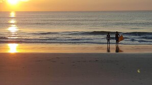 Escena de playa con dos personas cerca del agua, una sosteniendo una tabla de surf.