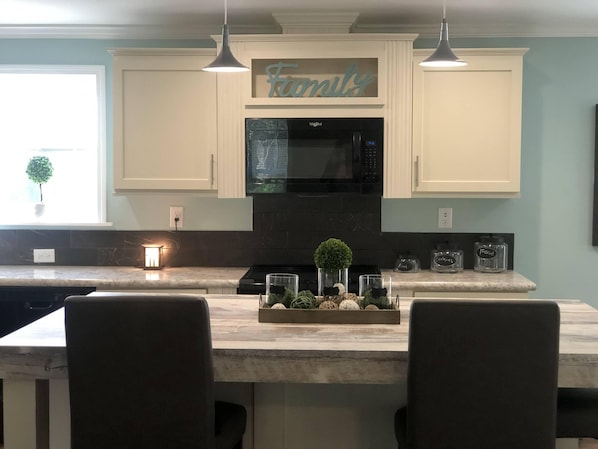 A kitchen with a central island, white cabinets, a black microwave, and a 'Family' sign above the cabinets.