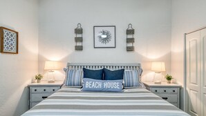 Une chambre à coucher comprenant un lit, deux tables de chevet, deux lampes fixées au mur, un tableau encadré et une porte.