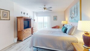 Un dormitorio con cama, televisión, ventilador de techo, ventana y obras de arte en las paredes.