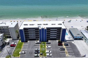Een meerhoog hotel met een parkeerplaats, uitzicht op het strand en een dakterras met parasols.