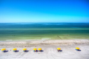 Een strand met rijen ligbedden en parasols, een heldere blauwe lucht en rustige oceaan.