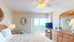 Habitación de hotel con cama, televisor, cómoda y balcón con vista al océano.
