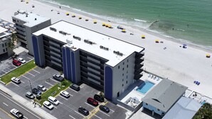 Un hotel de varios pisos con piscina en la azotea, estacionamiento y vista al mar.