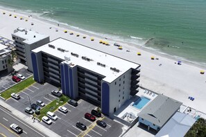 A multi-story hotel with a rooftop pool, parking lot, and a beach view.