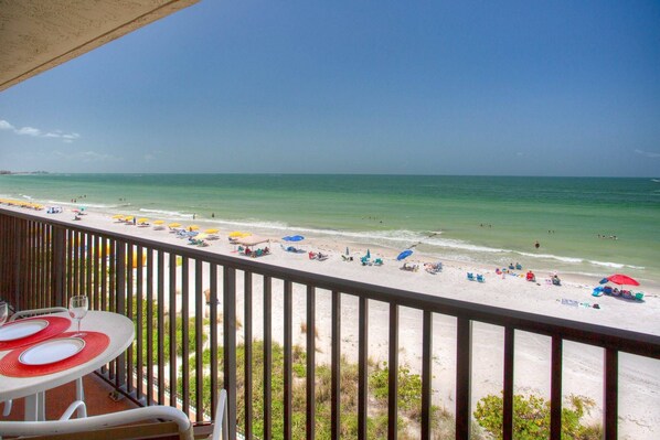 Een balkon met uitzicht op een strand met parasols en mensen.
