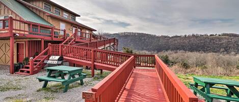Una terraza de madera con mesas de picnic, una escalera roja y vistas a una colina boscosa.