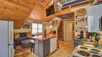 A cozy cabin interior with a kitchen, dining area, and a loft bedroom.