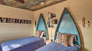 Une chambre avec deux lits, chacun doté d’une tête de lit bleue et d’oreillers à motifs. Une pancarte sur le mur indique : « E Bait ».