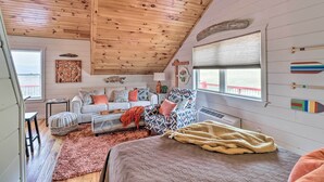 A cozy cabin interior with a wooden ceiling, a sofa, a patterned armchair, and a bed with a blanket. - Cheery Pet-Friendly Studio w/ Shared Fire Pit (Mountain View)