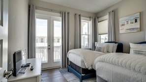 Ein Hotelzimmer mit zwei Betten, einem Schreibtisch mit Fernseher und einem Balkon mit Vorhängen.