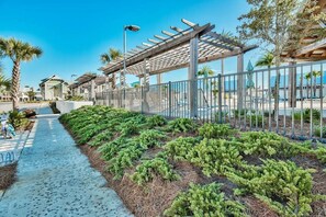 A pathway lined with green shrubs and a pergola structure. - Charming 30A Getaway, Bikes, Steps to Pool, Near Beach ~ Pearl Lighthouse 30A (Inlet Beach)