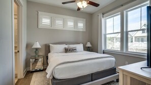 A bedroom with a bed, bedside lamps, a ceiling fan, and a large window. - Charming 30A Getaway, Bikes, Steps to Pool, Near Beach ~ Pearl Lighthouse 30A (Inlet Beach)