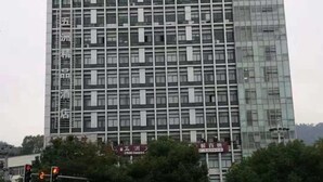 Ein mehrstöckiges Gebäude mit einer rasterartigen Fassade, das zahlreiche Fenster und ein zentrales vertikales Element aufweist.