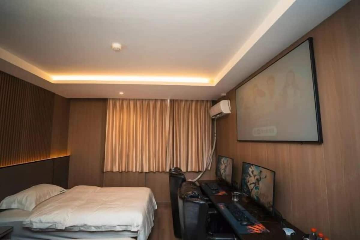 Een hotelkamer met een bed, een bureau met een computer, een stoel, een televisie en een raam met gordijnen.