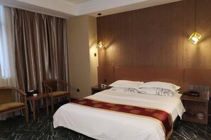 A hotel room with a large bed, two bedside tables, a wooden headboard, a window with curtains, and two wall-mounted lamps.
