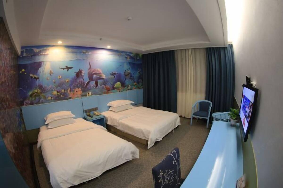 Een hotelkamer met twee bedden, een bureau, een televisie en een muurschildering met een zeemeer thema.
