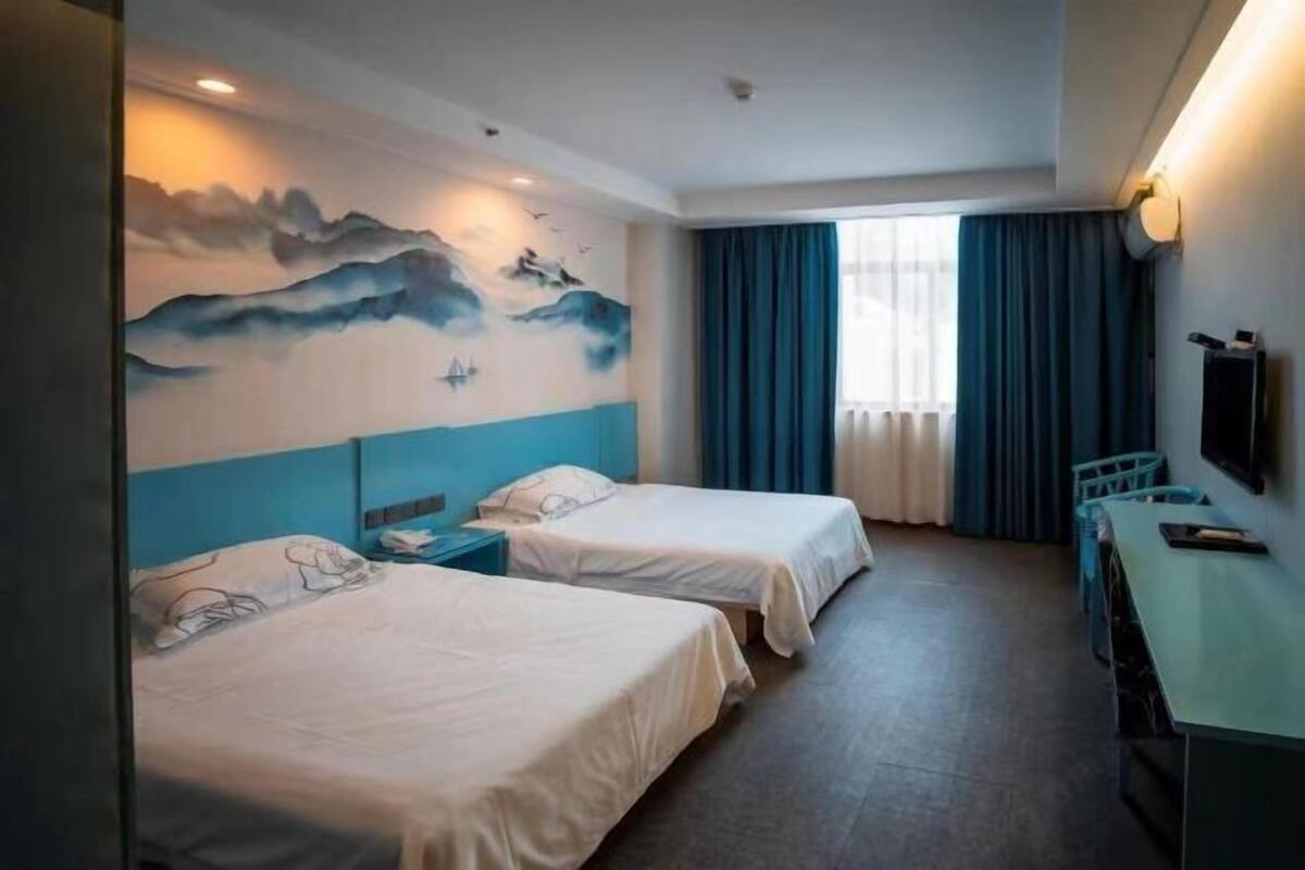 Een hotelkamer met twee bedden, een bureau, een televisie en een muurschildering.