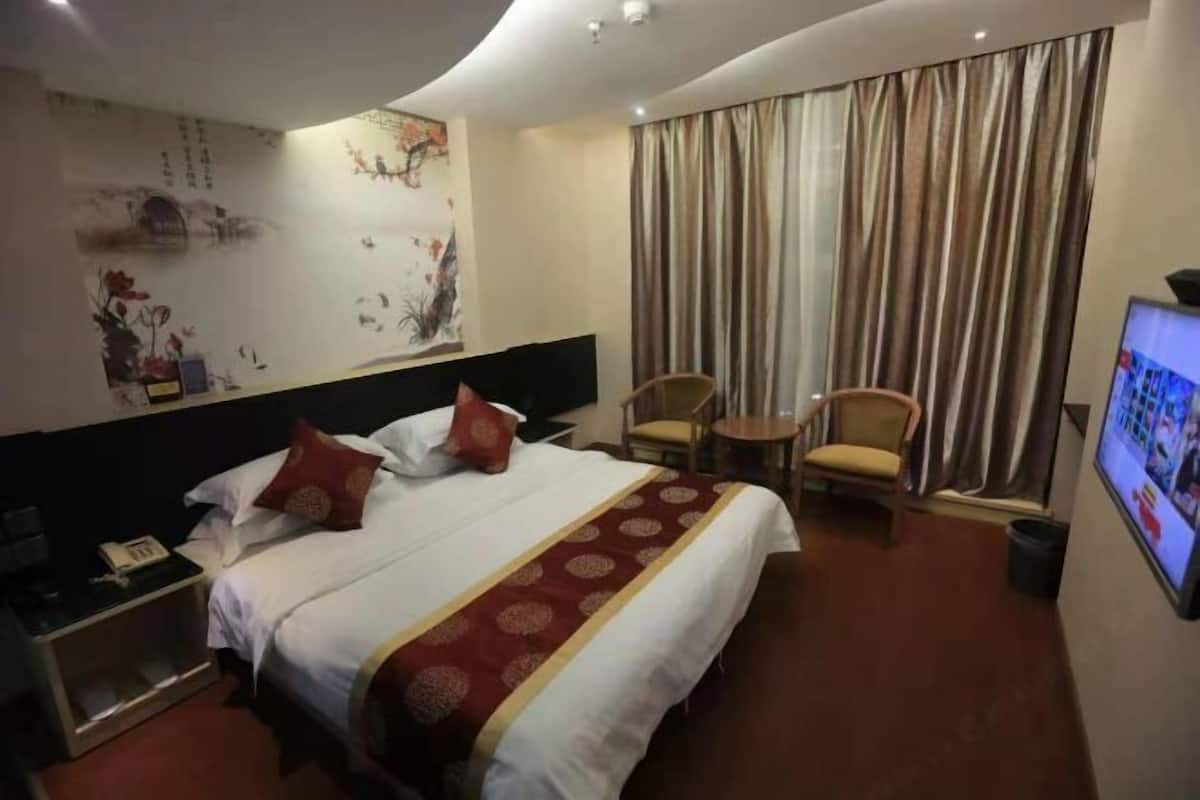 Een hotelkamer met een bed, een bureau, een stoel, een televisie en een gordijn.
