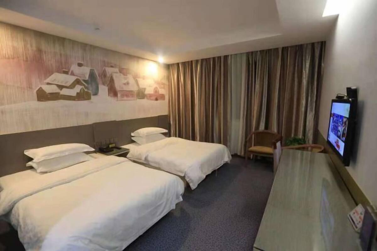 Een hotelkamer met twee bedden, een bureau, een stoel, een televisietoestel en een muurschildering.