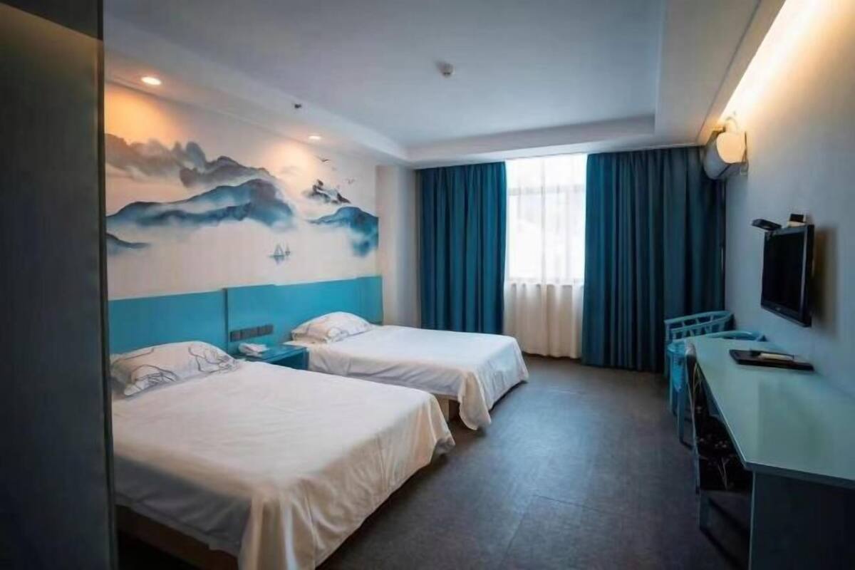 Hotelkamer met twee bedden, een bureau, een televisie en een muurschildering van bergen.