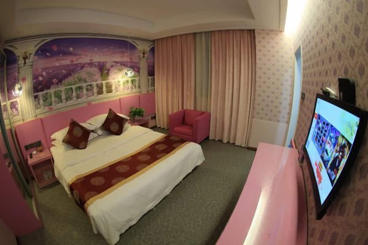 Een hotelkamer met een groot bed, een televisie, een roze stoel en een muurschildering.