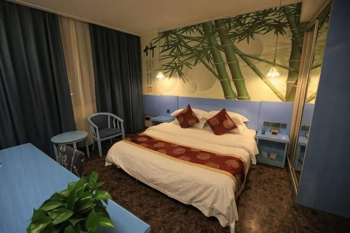 Een hotelkamer met een bed, een klein tafeltje, een stoel, een plant en een wand met een bamboemuurtekening.
