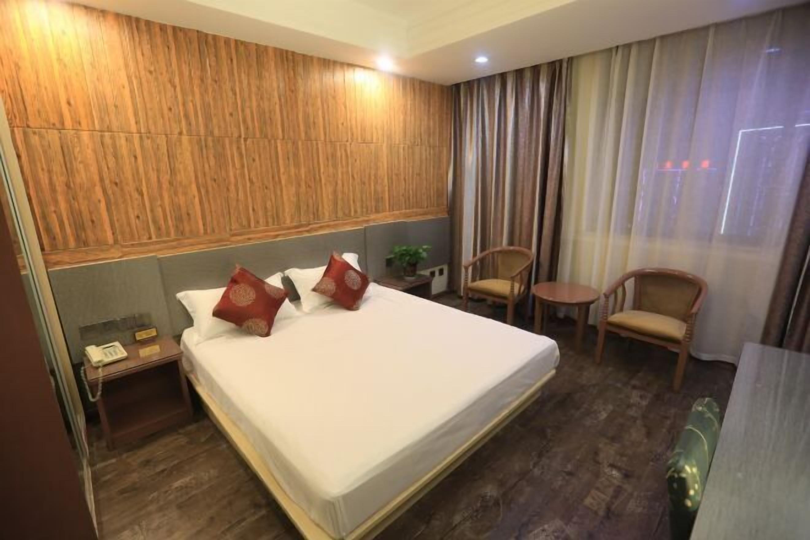 A hotel room with a large bed, wooden headboard, two chairs, a small table, and a bedside telephone.