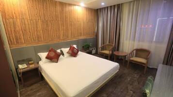 A hotel room with a large bed, wooden headboard, two chairs, a small table, and a bedside telephone.