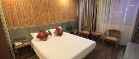 A hotel room with a large bed, wooden headboard, two chairs, a small table, and a bedside telephone.
