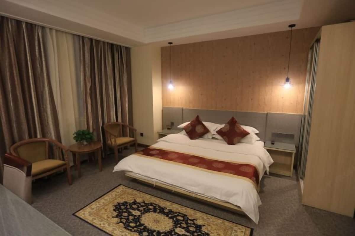Een hotelkamer met een bed, een bureau, een stoel, een nachtkastje en een groot raam met gordijnen.