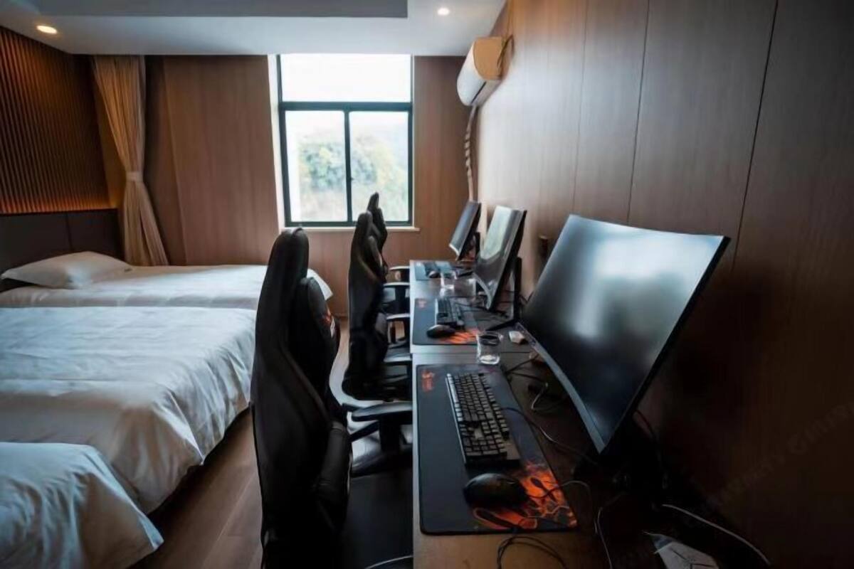 Een hotelkamer met twee bedden, een bureau met een computer en een groot raam.