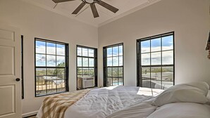 Une chambre à coucher avec un grand lit, trois fenêtres et un ventilateur de plafond.