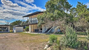 Une maison moderne à deux étages, dotée d’un balcon, entourée d’un jardin aménagé avec différents arbustes et un petit arbre.