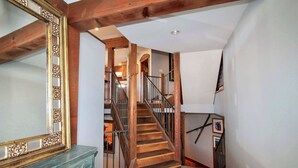 Una escalera de madera con barandilla metálica, un espejo con marco decorativo y un aparador de madera.