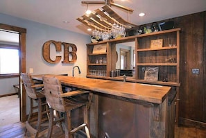 A bar area with a wooden bar counter, stools, and a shelf with glasses and bottles. - Sunlight Ridge Retreat, Luxury, Hot tub, Views! (Mt. Crested Butte)
