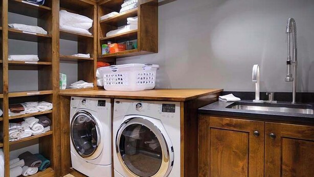 Un cuarto de lavado con dos lavadoras de carga frontal, estantes de madera con toallas dobladas y un lavamanos con grifo.