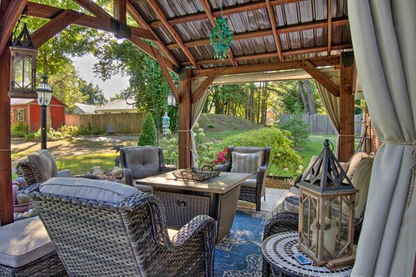 A covered outdoor seating area with wicker furniture, a table, and lanterns. - Charming Florence Getaway w/ Fireplace & Grill! (Florence)
