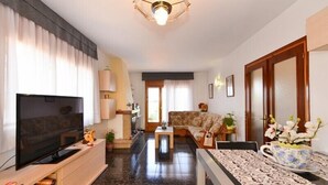 Una sala moderna con televisor de pantalla plana, sofá, una mesita de centro y un comedor con mantel estampado.