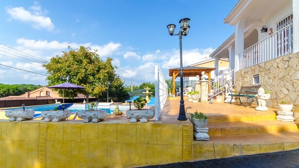 Un área de piscina con macetas de piedra, una pérgola y mobiliario de exterior.