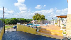 Zona de piscina con terraza cercada, plantas en macetas y pared de piedra.