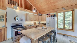 Una cuina moderna amb armaris de fusta, una illa gran, electrodomèstics d'acer inoxidable i vistes a la forest a través de grans finestres.