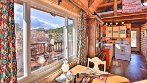 A cozy cabin interior with a large window offering a scenic view, a wooden dining area, and a kitchen with a stove. - Remote Escape w/ Deck & Sweeping Mountain Views! (Cotopaxi)