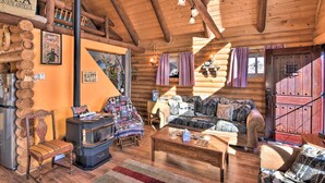 A rustic cabin interior with a wooden ceiling, a sofa, a chair, a table, and a wood-burning stove. - Remote Escape w/ Deck & Sweeping Mountain Views! (Cotopaxi)