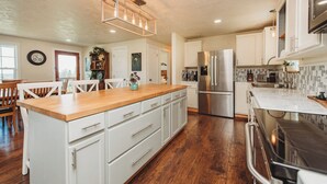 A spacious kitchen with wooden flooring, white cabinetry, a central island, stainless steel appliances, and a pendant light fixture. - Charming Hilltop Getaway - Valley and Water Views (Sequim)