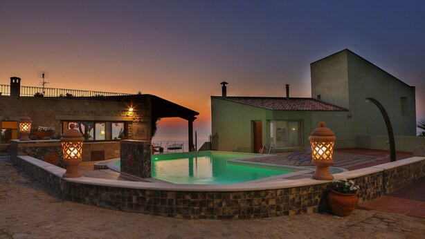 Une piscine bordée de pierres, entourée d’immeubles, avec un coucher de soleil en arrière-plan.