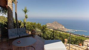 Une terrasse avec une table et des chaises, offrant une vue sur un paysage côtier caractérisé par une formation rocheuse imposante et la mer.